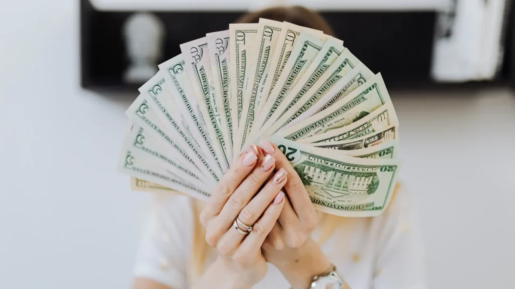 A person holding a fan of US dollar bills, symbolizing a high-paying digital marketing coordinator salary.
